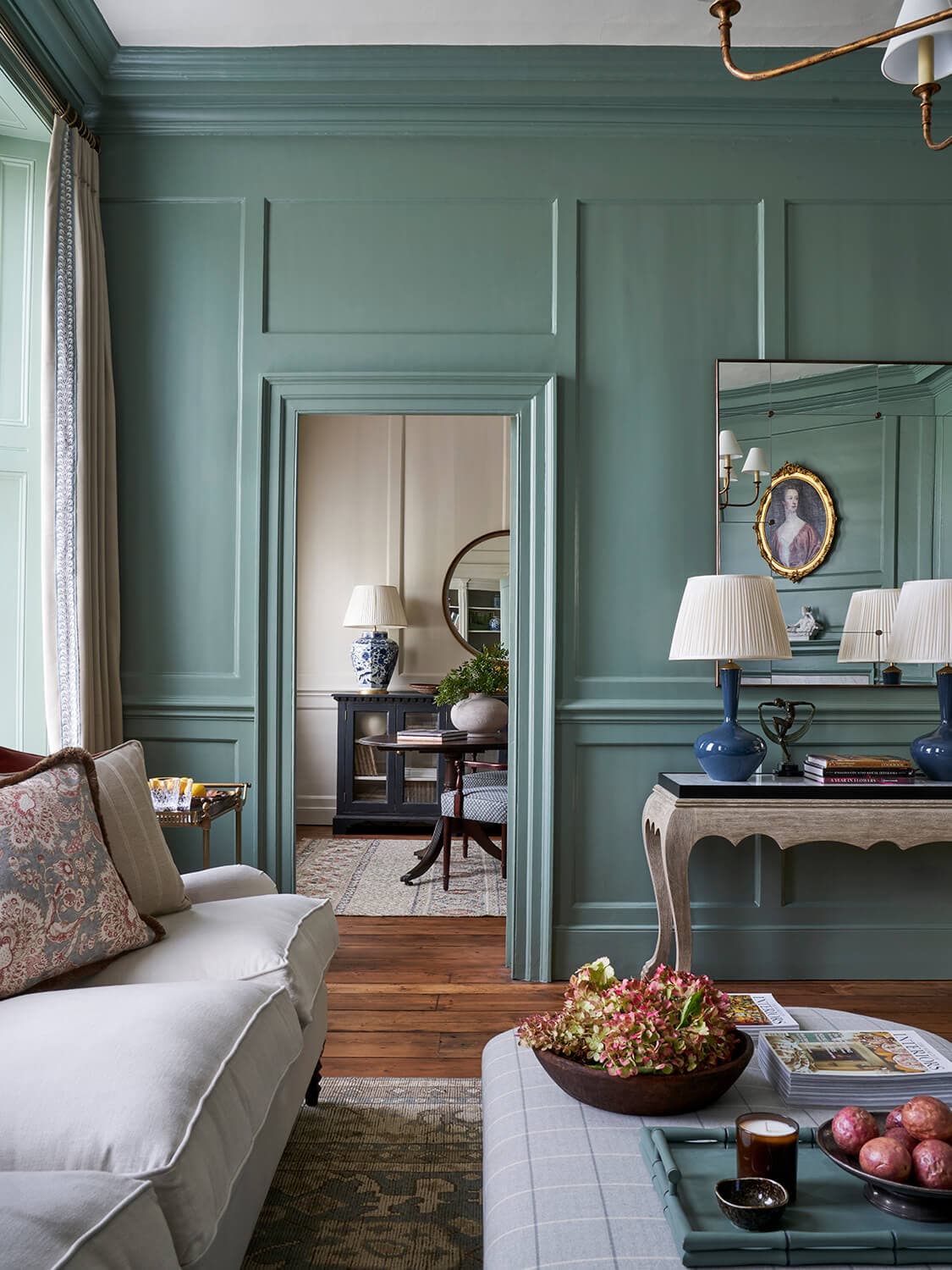 Soft green panelling in the drawing room of a Grade I listed London house, with a doorway through to the room beyond