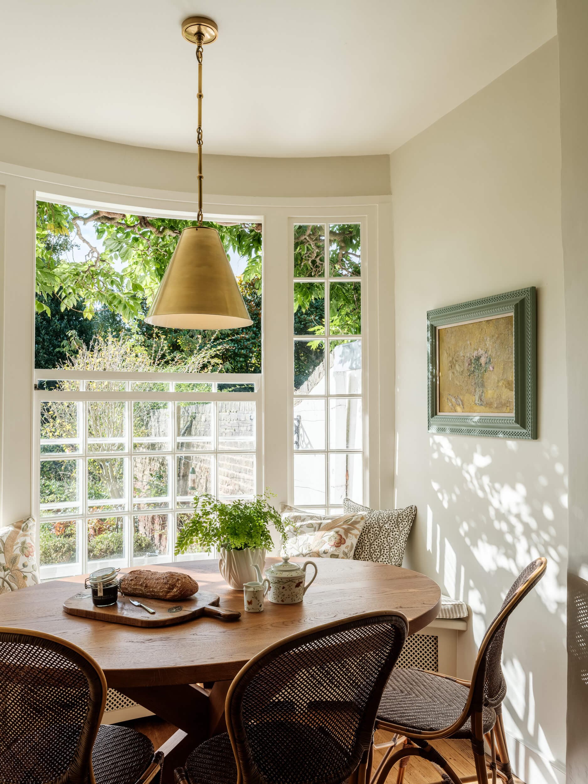 Kitchen breakfast nook in a curved bay window, with a round oak table, cane chairs and a brass pendant above