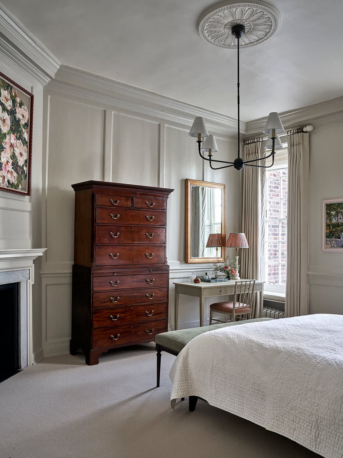 Principal bedroom in pale panelling, with an antique mahogany tallboy, a gilt mirror above a writing desk and a marble fireplace