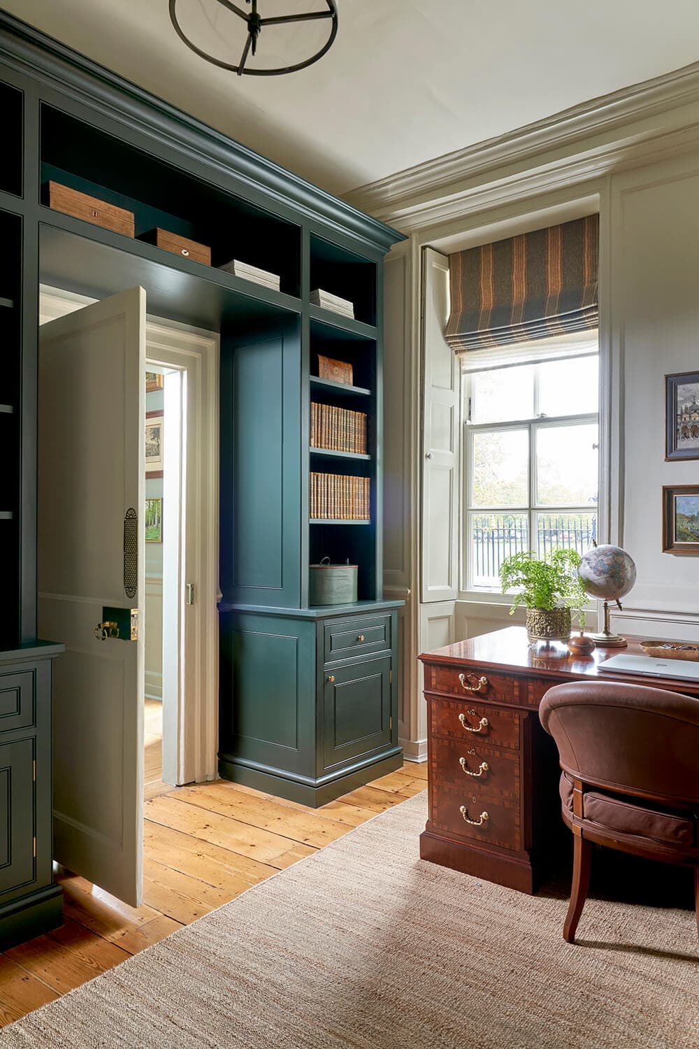 Study lined with bespoke joinery bookcases painted in a deep heritage green, beside a sash window and an antique desk